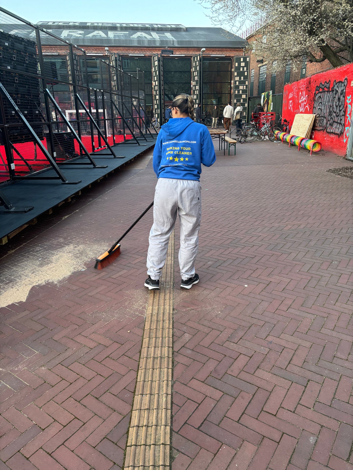 Worker sweeping a brick pathway at a venue, preparing for an event cleaning service in Copenhagen.