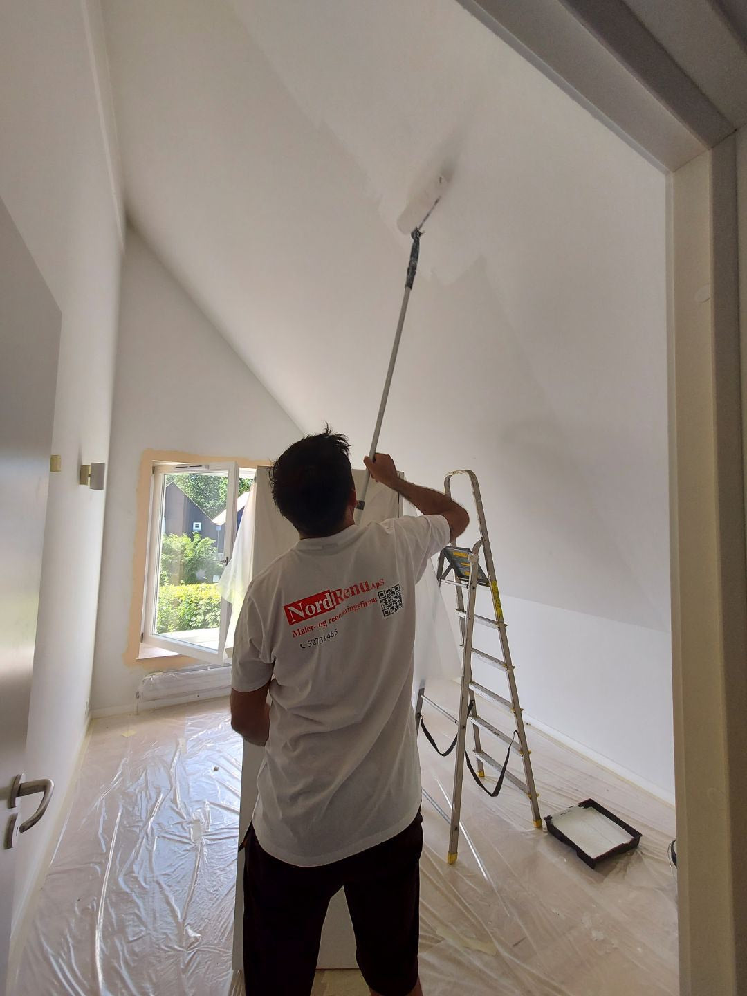 Professional wall painting service in Copenhagen, featuring a worker painting a ceiling.